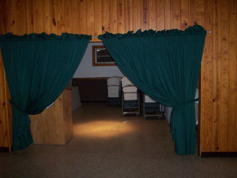 1985 Ford Bronco - A view through green curtains reveals stacked chairs and a wooden-paneled room, suggesting a venue setup.