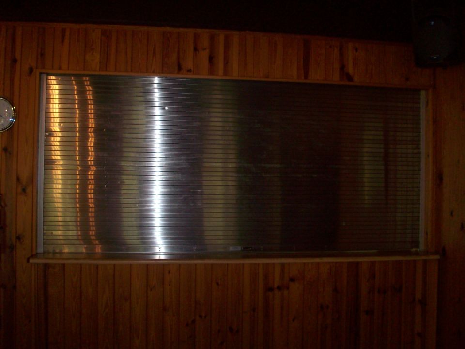 Window with horizontal metal blinds behind a wooden counter, set into a wood-paneled wall