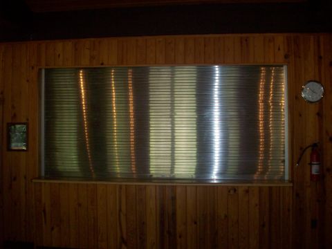 1985 Ford Bronco - A clock hangs on a wood-paneled wall next to a window covered by horizontal blinds.