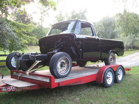 1966 Ford F-100 - A black 1966 Ford F-100 pickup truck is being transported on a red trailer, with its front end appearing to be under repair.