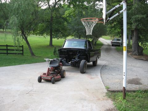 1966 Ford F-100 - A black pickup truck body sits on a driveway, awaiting restoration, with a riding mower nearby.