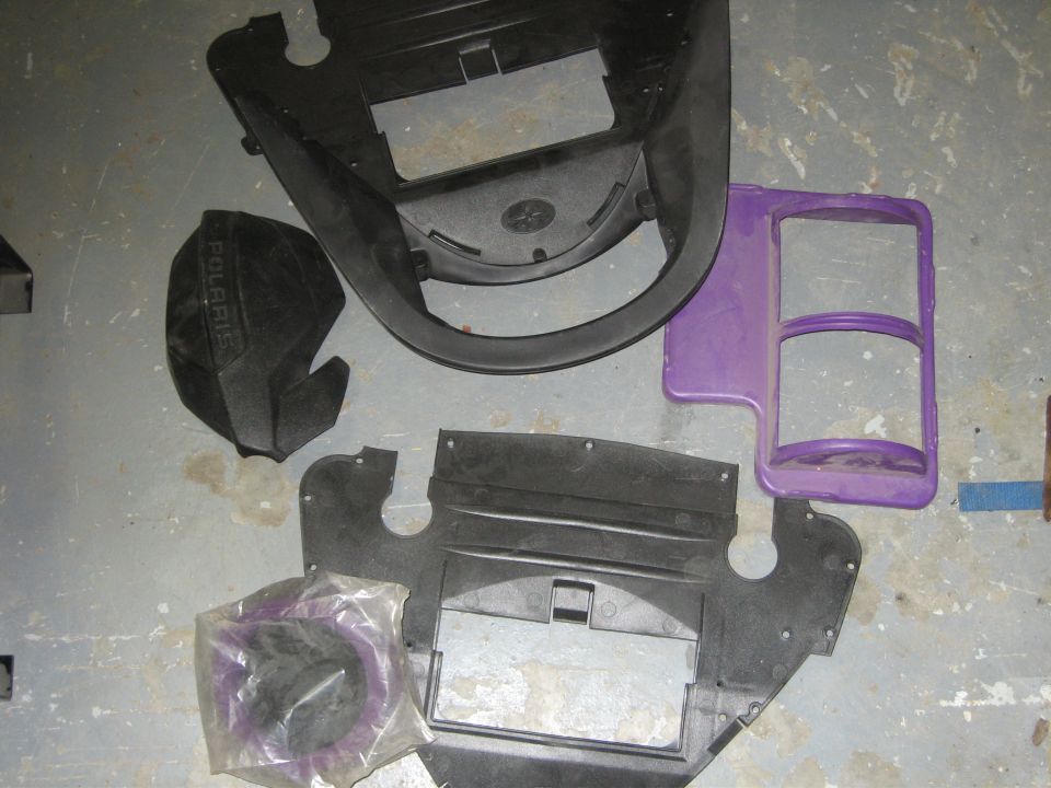 ATV body panels on concrete floor: black plastics, a Polaris-branded cover, and a purple headlight pod housing
