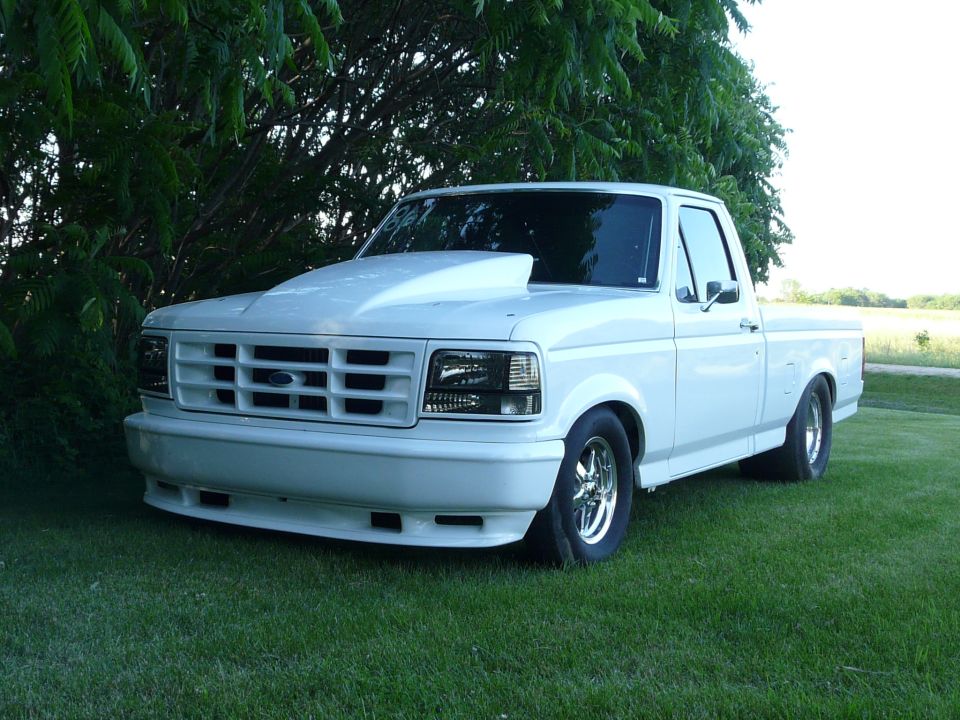 Lowered white Ford pickup with cowl hood scoop and skinny front tires parked on grass
