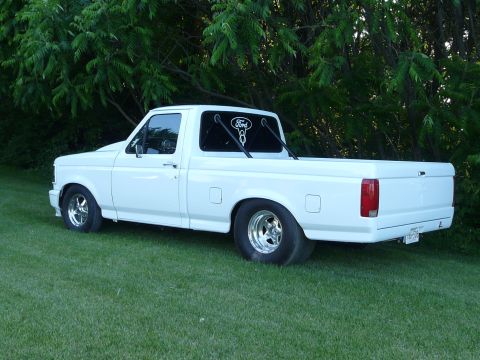 1994 Ford F-150 - This white 1994 Ford F-150 pickup truck is shown from the rear 3/4 angle, a custom roll bar and aftermarket wheels.