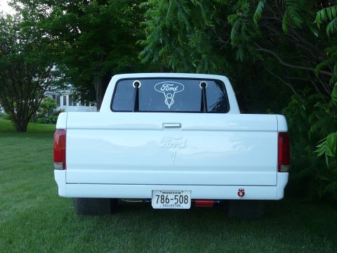 1994 Ford F-150 - Straight-on rear view of a white Ford pickup parked on a grass lawn, showing the smooth tailgate with debadged Ford script outline, a Ford…