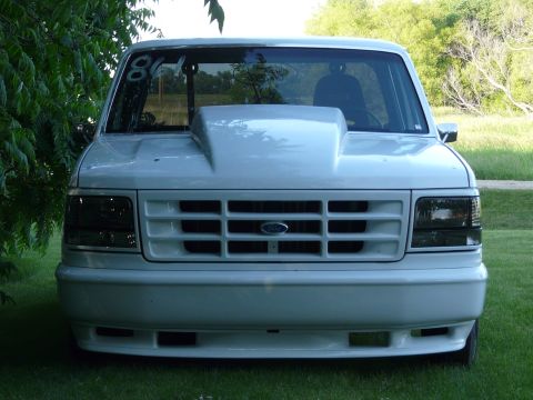 1994 Ford F-150 - Front view of a white pickup truck a prominent aftermarket hood scoop and a number written on the windshield.