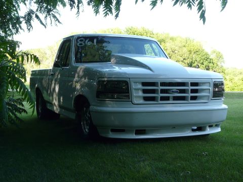 1994 Ford F-150 - This white pickup truck has a prominent hood scoop and a grille consistent with the early 1990s Ford F-150 model.