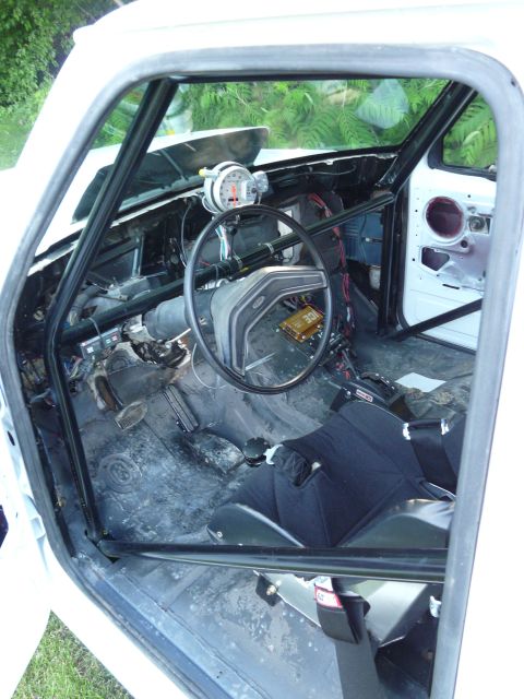 1994 Ford F-150 - The interior of a white truck shows a roll cage, racing seat, and a tachometer mounted on the dashboard.