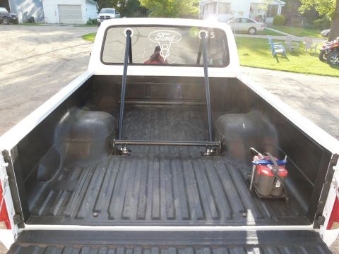 1994 Ford F-150 - The bed of a 1994 Ford F-150 shows a custom rack and a spare battery. The Ford logo is visible on the rear window.