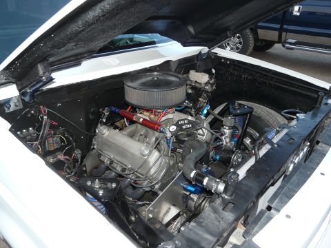 1994 Ford F-150 - The engine bay of a white vehicle is shown, with a V8 engine and custom modifications. Another vehicle is parked behind it.