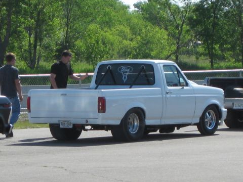 1994 Ford F-150 - Three-quarter rear view of a lowered white Ford regular-cab pickup in a race-track pit area, running fat rear drag tires on polished wheels…