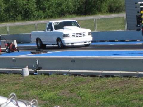 1994 Ford F-150 - A white 1994 Ford F-150 pickup truck, modified with a hood scoop, sits on a drag strip.
