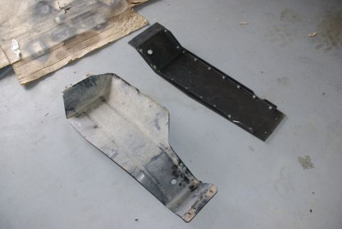 1995 Ford Bronco - Two shop-fabricated steel skid plates lying face-up and face-down on a concrete garage floor next to a cardboard template. The welded, boxe…