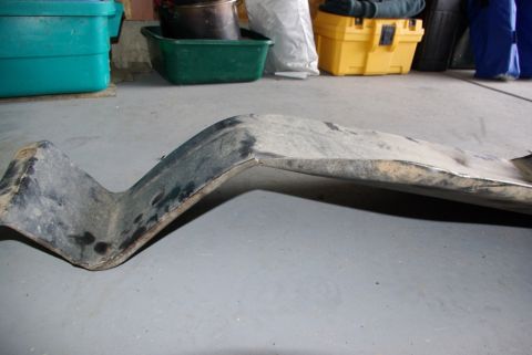 1995 Ford Bronco - A bent metal skid plate rests on a concrete floor, with various storage containers visible behind it.