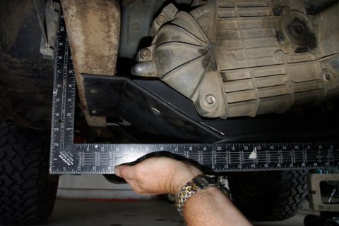 1995 Ford Bronco - Underbody shot of a truck on a garage floor with a hand holding a framing square against the newly installed black skid plate to check grou…
