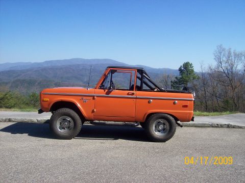 1973 Ford Bronco - Side view of an orange 1973 Ford Bronco with a roll bar, parked outdoors.