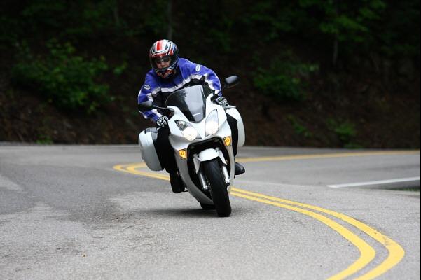 Motorcyclist wearing a helmet and blue jacket riding a white touring motorcycle on a winding road
