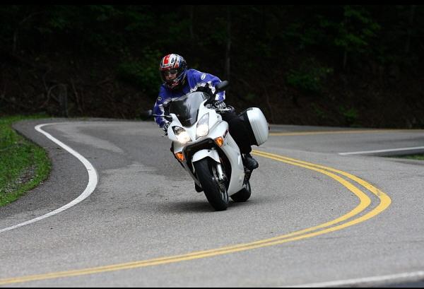 Motorcyclist in blue jacket and helmet leans into a turn on a white sportbike with saddlebags