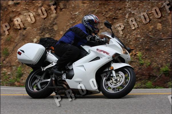 White motorcycle with saddlebags on a road, rider wearing a helmet and blue jacket
