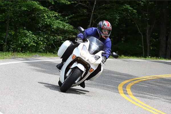 Rider on white sport touring motorcycle leaning into a curve on a road with yellow double lines