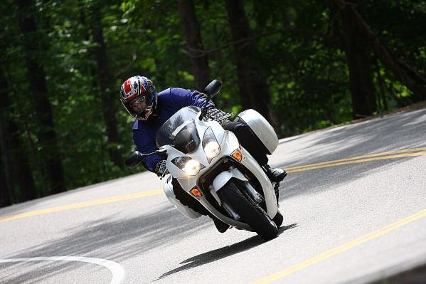 Motorcycle rider leans into a curve on a tree-lined road