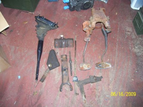 1978 Ford Bronco - Assorted vehicle parts, including pedals and a shifter boot, are displayed on a floor.
