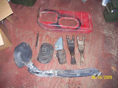 1978 Ford Bronco - Various automotive parts, including a red door panel and exhaust components, are laid out on a red floor.