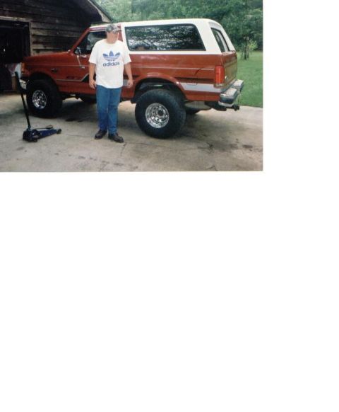 1987 Ford Bronco - A man stands beside a red and white 1987 Ford Bronco parked on a concrete driveway.