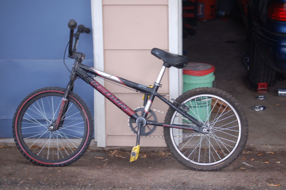 Black Redline BMX bicycle with red accents on wheels and frame, parked outdoors