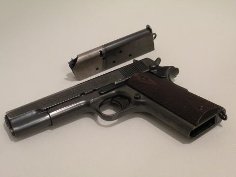 1996 Ford Bronco - A Colt M1911 pistol and its magazine are displayed on a plain surface.