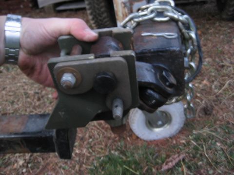 1996 Ford Bronco - A hand grips a trailer hitch mechanism, showing its intricate parts and attached chains, with a small wheel visible below.