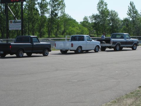 1994 Ford F-150 - Three pickup trucks are lined up on a paved surface, with trees and a sign in the background.