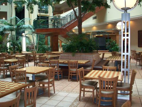 1985 Ford Bronco - An indoor atrium features numerous tables and chairs, some with checkerboard tops, set amidst lush greenery and a central staircase.