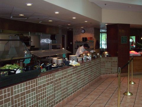 1985 Ford Bronco - A person in a white shirt and hat arranges food on a buffet line in a hotel dining area.