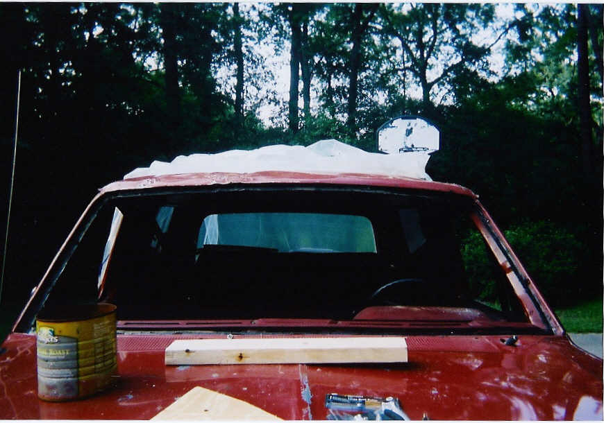 Red 1987 Ford Bronco with windshield removed, plastic sheeting on roof, coffee can and board on hood