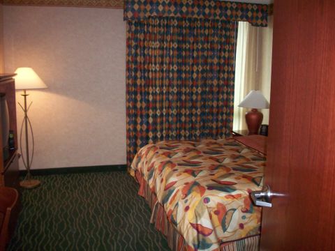 1985 Ford Bronco - Interior view of a hotel room a bed with colorful bedding, patterned curtains, and a floor lamp.