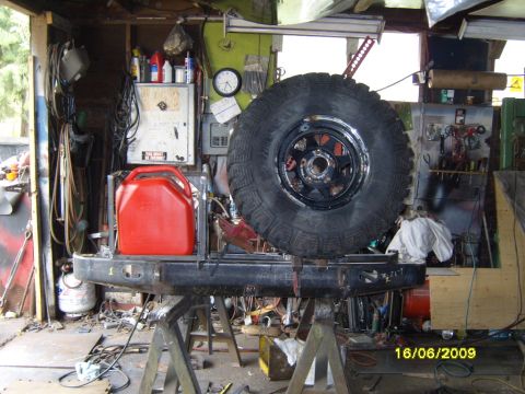 1989 Ford Bronco - A vehicle's rear bumper, spare tire, and gas can are assembled in a workshop.