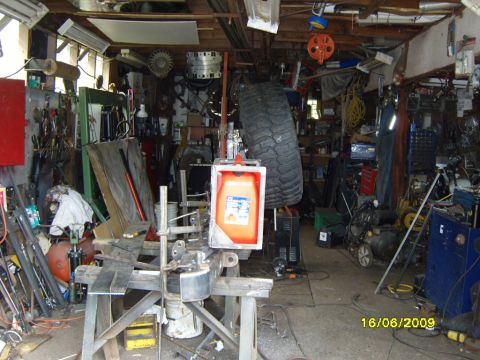 1989 Ford Bronco - A cluttered garage scene shows various tools, a large spare tire, and an orange gas can hanging from a hoist.