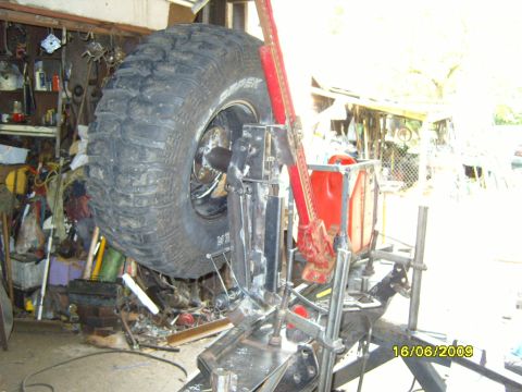 1989 Ford Bronco - A large tire is mounted on a jack with various tools and parts in the background.