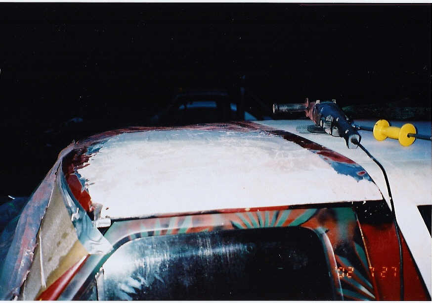 Roof of a Bronco coated in white body filler at night, with tools on top and airbrushed graphics visible below