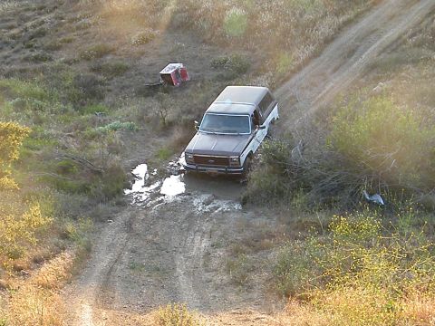 1982 Ford Bronco - A two-tone Ford F-Series truck navigates a muddy trail in a dry, grassy area.
