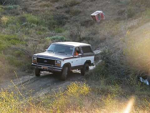 1982 Ford Bronco - A two-tone white and brown Ford Bronco navigates a dusty trail surrounded by dry brush.