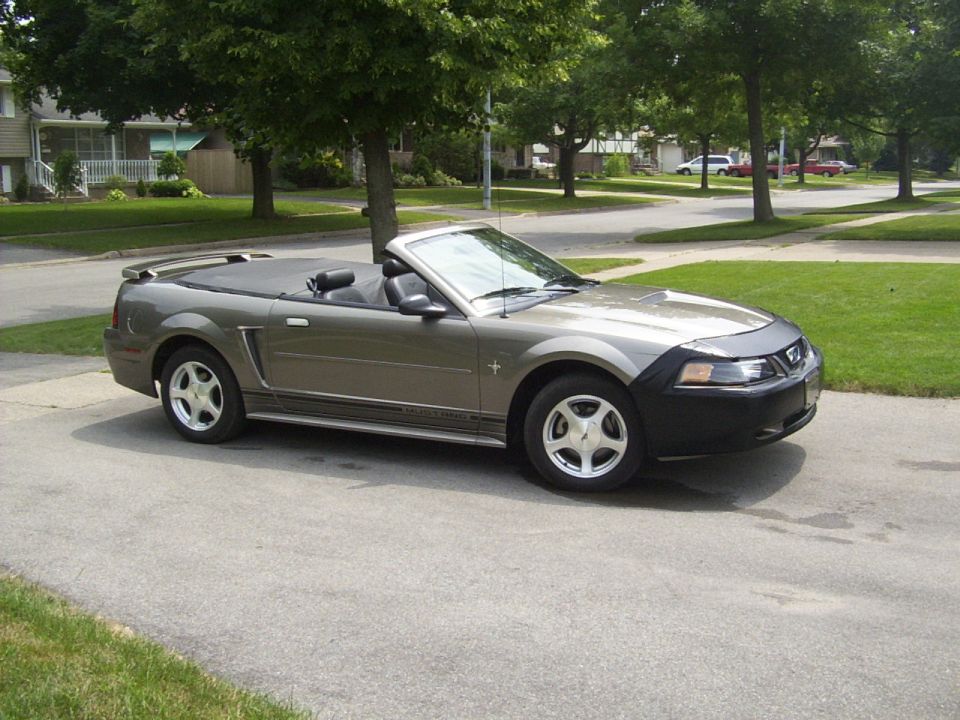 Gray Ford Mustang convertible, top down, 3/4 front view parked in a suburban driveway.