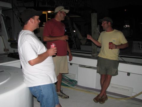 1979 Ford F-150 - Three men are gathered on a boat's deck in the evening, each holding a beverage.