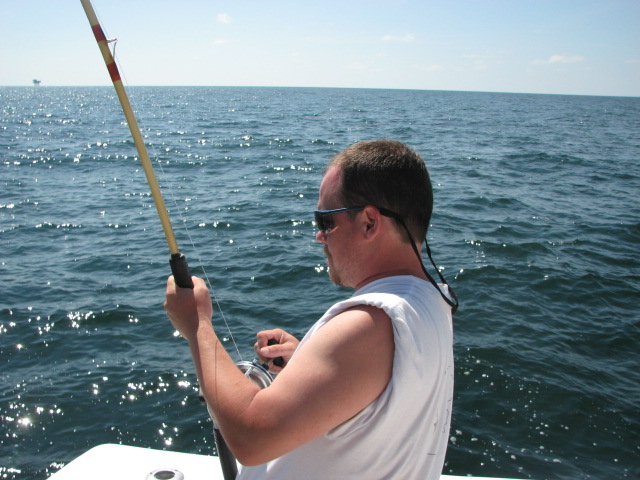 Man in white t-shirt and sunglasses fishes from a boat on the ocean