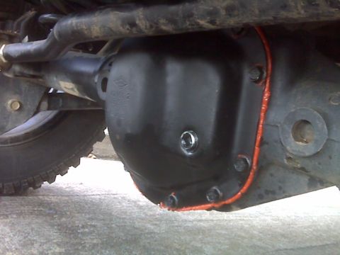 2008 Jeep Wrangler - Underside close-up of a black cast differential cover freshly sealed with a bead of red RTV silicone squeezed out around the bolted flange.…