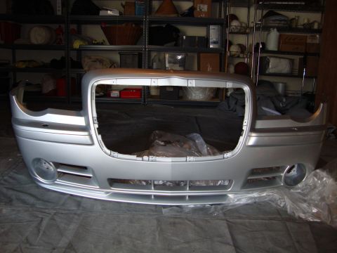 2008 Chrysler 300 - A silver Chrysler 300 front bumper assembly is shown, missing its grille and headlights, in a storage area.