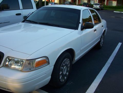 2003 Ford Crown Victoria - A white sedan is parked in a parking lot next to a white pickup truck.