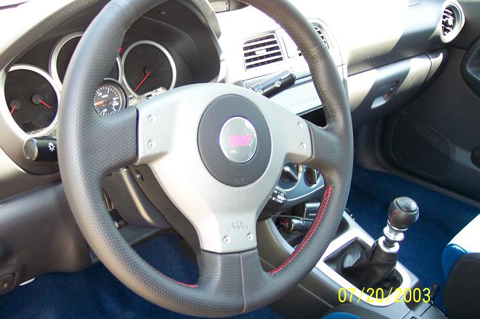 Subaru interior showing STI steering wheel, gauges, and manual shifter. Date stamp reads 07/20/2003