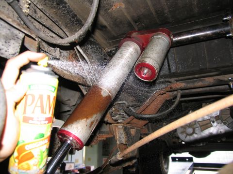 1984 Ford Bronco - A can of PAM cooking spray is used to lubricate a rusty shock absorber on the underside of a vehicle.